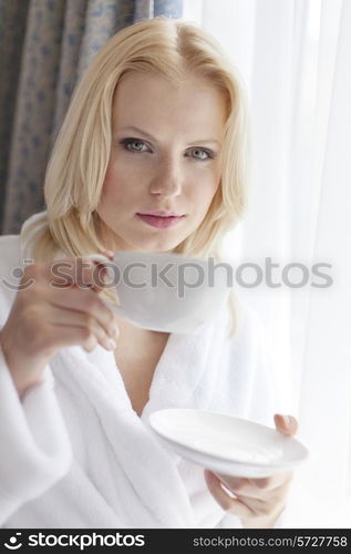 Portrait of attractive young woman in bathrobe drinking coffee at hotel room