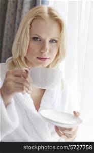 Portrait of attractive young woman in bathrobe drinking coffee at hotel room