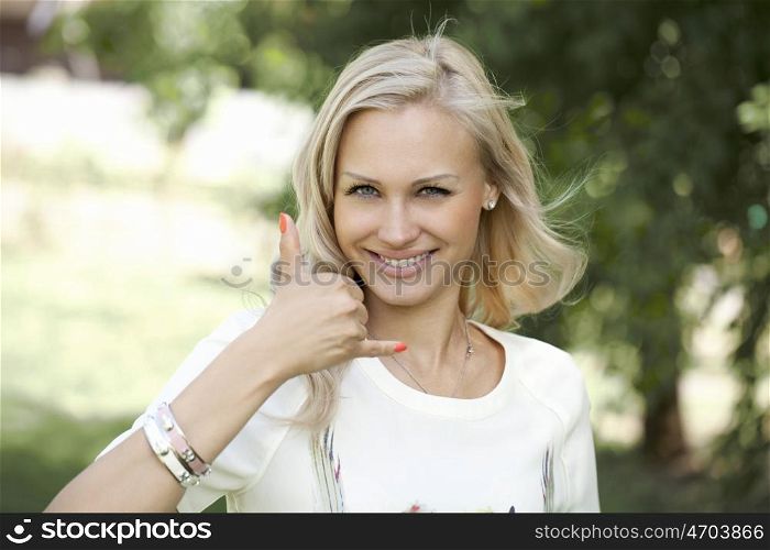Portrait of attractive young woman on open air. Woman making a call me sign outdoors