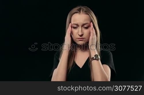 Portrait of attractive young woman suffering from headache grimacing in pain with hands on her temples against black background. Beautiful girl massaging her temples, easing her headache pain tension migraine.