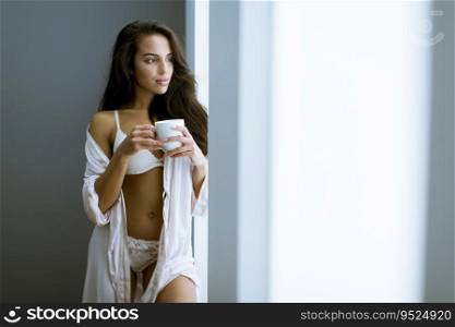 Portrait of attractive young woman with mug by the window in bedroom