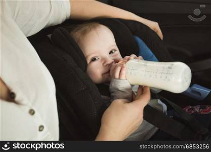 Portrait of baby boy drinking milk from bottle on car back seat