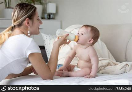 Portrait of baby boy sitting on bed and eating milk from bottle