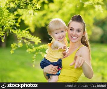 Portrait of baby girl and smiling mother pointing in camera