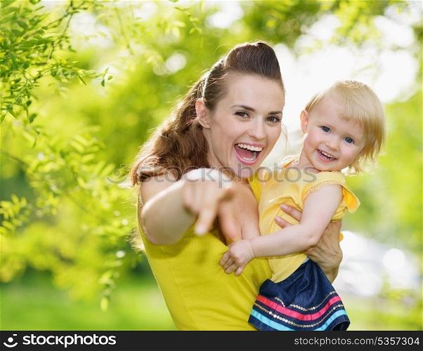 Portrait of baby girl and smiling mother pointing in camera