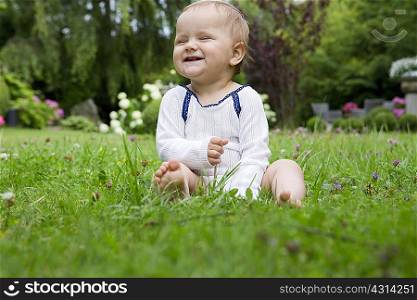 Portrait of baby girl sitting on lawn laughing