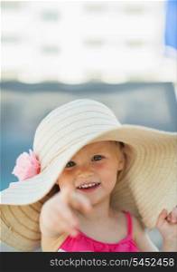 Portrait of baby in beach hat pointing in camera