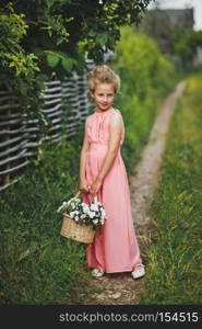 Portrait of baby in pink dress on the path at the wicker fence. Portrait of a child in a dress and with makeup on nature 6597.