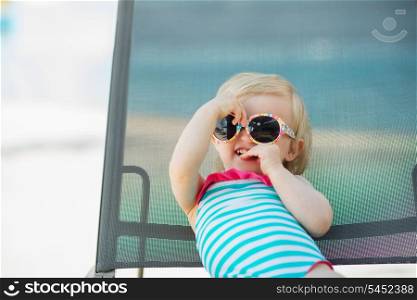 Portrait of baby in swimsuit and sunglasses laying on sunbed