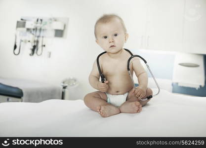 Portrait of baby sitting on an examination table in the doctors office with a stethoscope around his neck