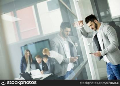 Portrait of beard businessman using mobile phone in office while other business people having meeting in background