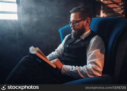 Portrait of bearded man in glasses sitting in armchair against window with sunlight in smoky room. Writer, journalist, literature author, blogger or poet concept. Man in glasses against window in smoky room