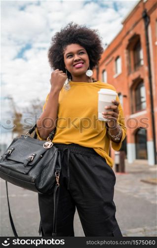 Portrait of beautiful afro american latin woman walking and holding a cup of coffee outdoors in the street. Urban concept.