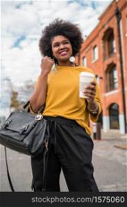 Portrait of beautiful afro american latin woman walking and holding a cup of coffee outdoors in the street. Urban concept.