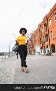 Portrait of beautiful afro american woman walking and holding a cup of coffee outdoors in the street. Urban concept.