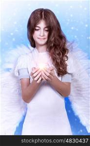 Portrait of beautiful angel, sweet teen girl wearing white dress and big fluffy wings on blue snowy background, holding candle, Christmas wish concept