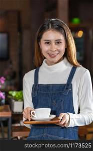 Portrait of beautiful asian barista holding cup of coffee in the cafe