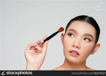 Portrait of Beautiful Asian woman holding makeup blusher brush. Skin care healthy hair and skin close up face beauty isolated over background. Cosmetology and Spa concept.
