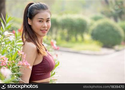 Portrait of beautiful Asian woman look at camera and stand near flower with background of road in park or garden also morning light.