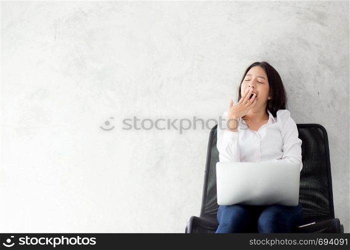 Portrait of beautiful asian young woman yawn at her work place with laptop computer on cement background, girl working freelance is a blogger with stress and tired, copy space.