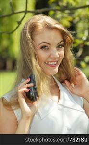 Portrait of beautiful, attractive blonde woman brushing her hair. Outdoor shot on sunny day. Outdoor portrait of beautiful blonde woman