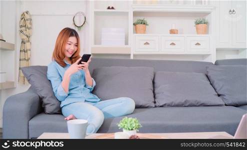 Portrait of beautiful attractive young smiling Asian woman using smartphone while lying on the sofa when relax in living room at home. Enjoying time lifestyle women at home concept.