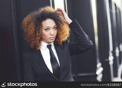 Portrait of beautiful black businesswoman wearing suit and tie in urban background. Model of fashion with afro hairstyle.