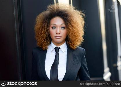 Portrait of beautiful black businesswoman wearing suit and tie in urban background. Model of fashion with afro hairstyle.