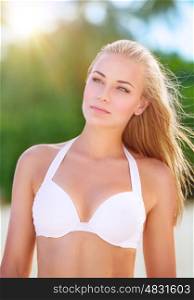 Portrait of beautiful blond girl on the beach standing on bright sun light, sexy model wearing stylish white swimsuit, fashion of summer time