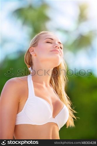 Portrait of beautiful blond girl on the beach with closed eyes of pleasure enjoying sunny day, sexy model wearing stylish white swimsuit, fashion of summer time