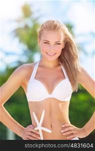 Portrait of beautiful blond model posing on the beach with starfish, luxury summer time photoshoot, having fun on beach resort