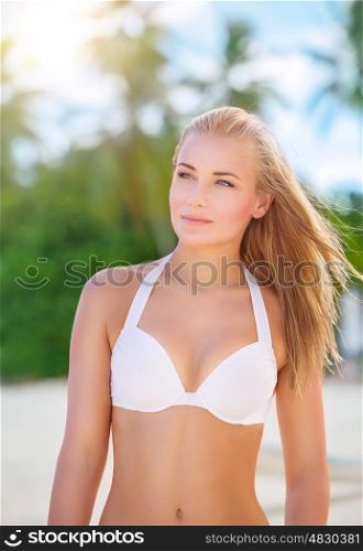 Portrait of beautiful blond woman on the beach, cute female wearing stylish white swimsuit, spending summer holidays on beach resort