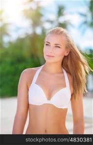 Portrait of beautiful blond woman on the beach, cute female wearing stylish white swimsuit, spending summer holidays on beach resort