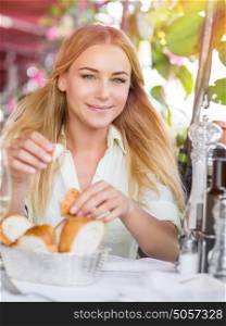 Portrait of beautiful blond woman sitting at outdoors cafe and eating bread, waiting for someone, spending summer vacation in Italy, Europe
