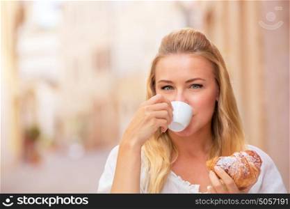 Portrait of beautiful blond woman sitting in outdoors cafe in Italy, drinking coffee and eating croissant, happy travel to Europe