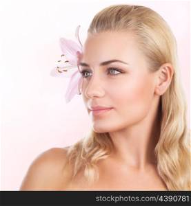 Portrait of beautiful blond woman with gentle pink lily flower in hair isolated on white background, looking on side, luxury spa salon