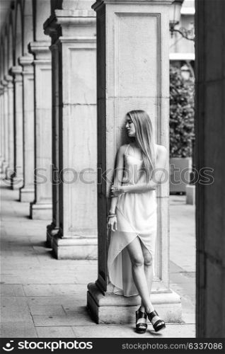Portrait of beautiful blonde girl in urban background wearing white dress