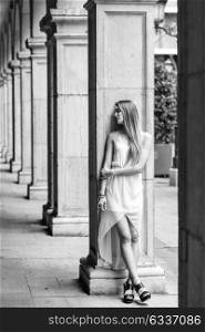 Portrait of beautiful blonde girl in urban background wearing white dress