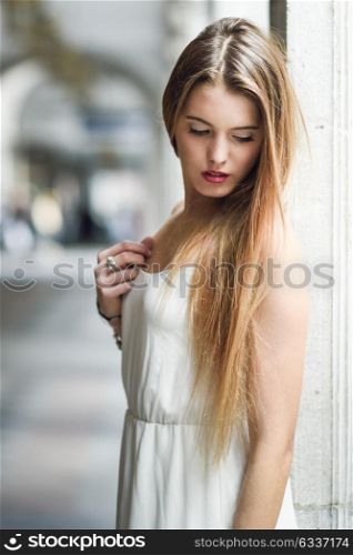 Portrait of beautiful blonde girl in urban background wearing white dress in urban background