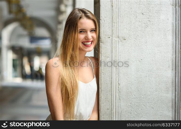 Portrait of beautiful blonde girl in urban background wearing white dress in urban background