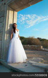 Portrait of beautiful bride in white dress near the old wall.