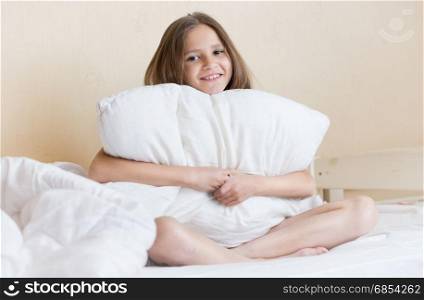 Portrait of beautiful brunette girl sitting on bed with white pillow