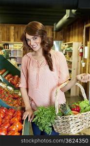 Portrait of beautiful brunette holding basket near tomato stall in market