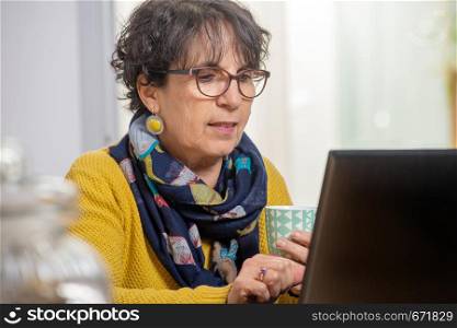 portrait of beautiful brunette mature woman wearing in yellow using a laptop