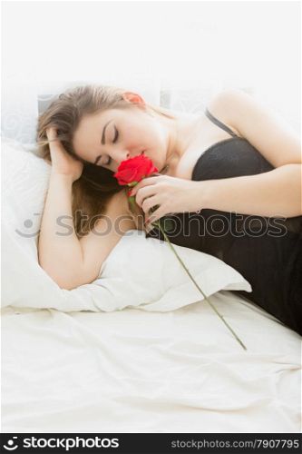Portrait of beautiful brunette woman posing with red rose in bed