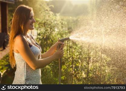 Portrait of beautiful brunette woman watering garden bed with vegetables