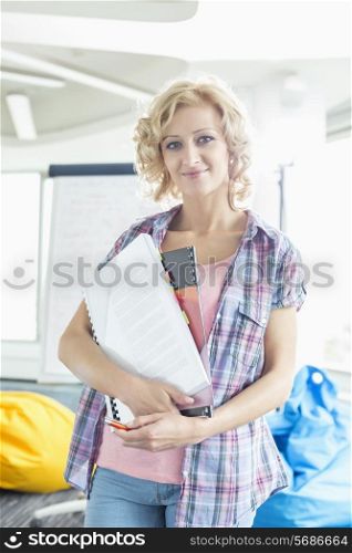 Portrait of beautiful businesswoman holding files in creative office