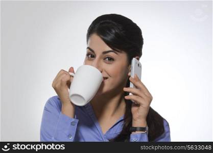Portrait of beautiful businesswoman using phone while having coffee against gray background