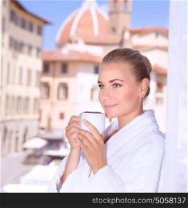 Portrait of beautiful calm woman drinking coffee in hotel room in Florence, Italy, Europe, standing on balcony on wonderful cityscape background