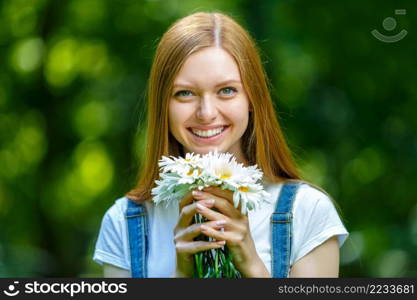 Portrait of beautiful caucasian smiling red-haired young woman, against summer green park.. Beautiful smiling red-haired young woman